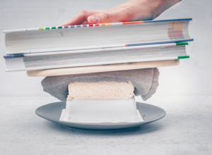 Lege nun ein Küchentuch zum Aufsaugen der Flüssigkeit und ein paar Schwere Bücher auf den Tofu. Die pressen die Flüssigkeit durch die Löcher im Sieb aus dem Tofu heraus. Tofu-pressen-schritt3