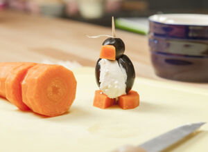 Ein Pinguin-Spieß steht auf einem Holzbrett